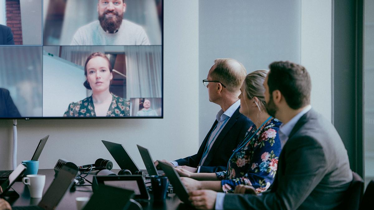 Ihmisiä kokoustamassa kokoustilassa, jossa myös videoneuvotteluyhteys muihin osallistujiin.