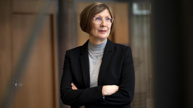 Harmaaseen pooloon ja mustaan jakkuun pukeutunut nainen katsoo haaveellisena oikealle etuviistoon. Taustalla tummahko puuseinä.